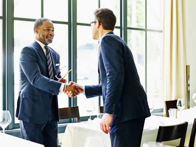 Two businessmen shaking hands at lunch meeting.